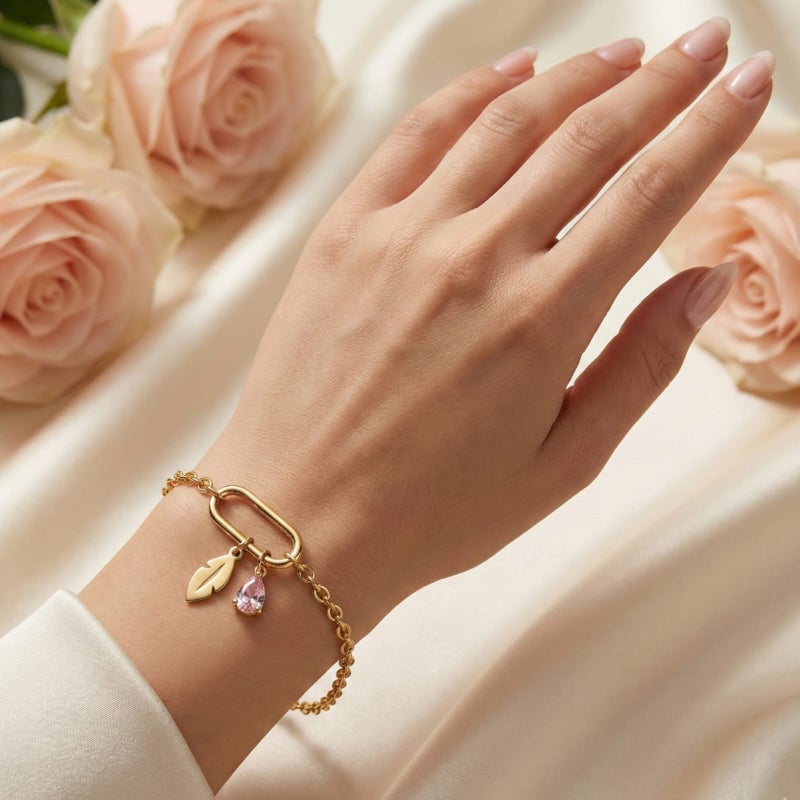 This attractive gold bracelet, crafted from rust-resistant stainless steel, features a modern link ring from which a delicate feather and a sparkling pink stone dangle. It has an adjustable clasp for a perfect fit. - Image 1